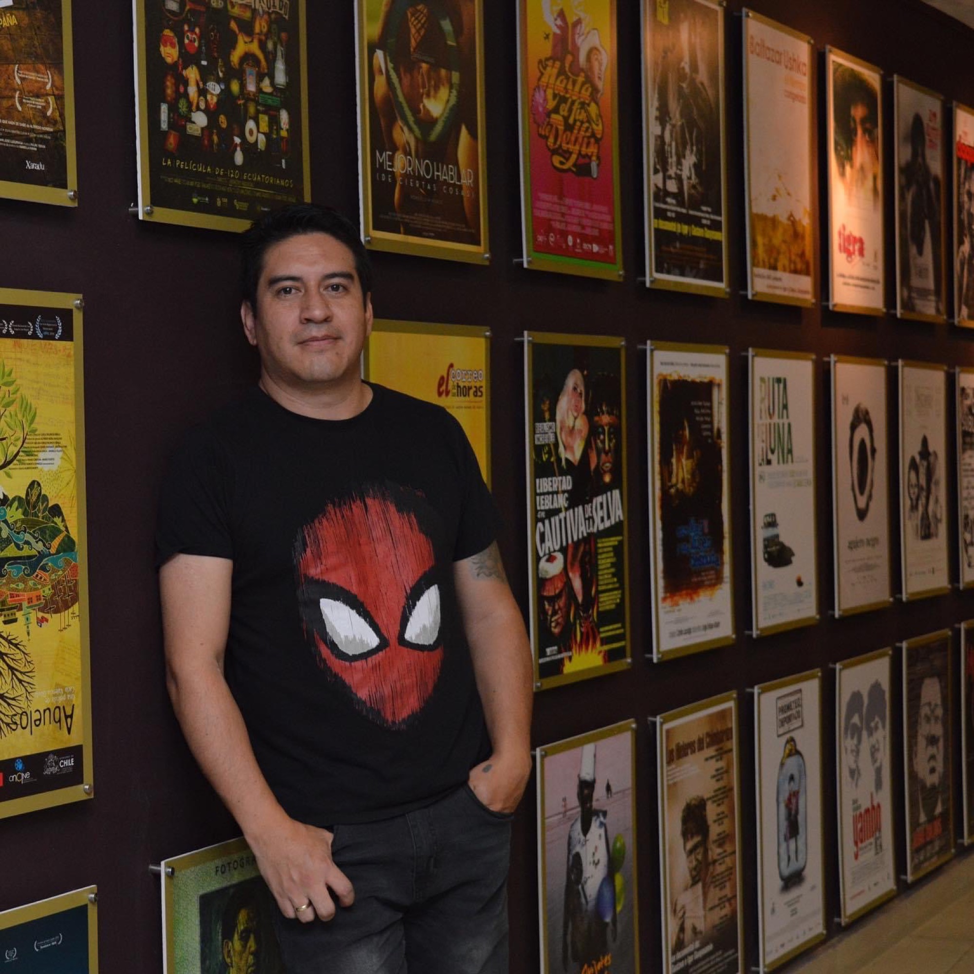 Edison Rodríguez Tapia standing in a gallery of Ecuadorian film posters